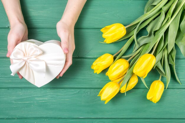 Persona con caja de regalo en forma de corazón cerca de tulipanes