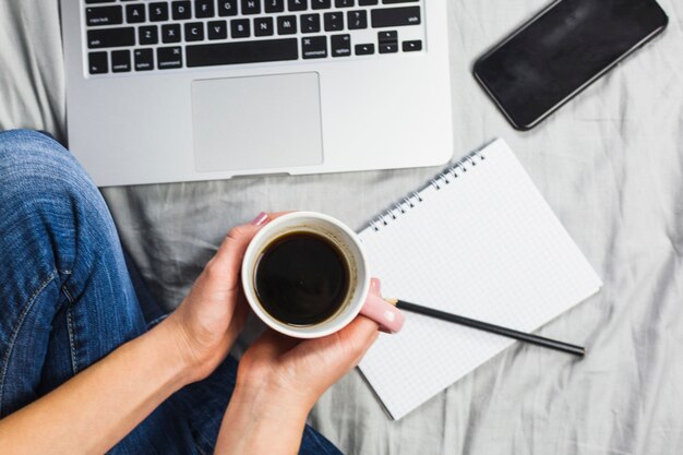 Persona en cama con taza de café y bloc de notas