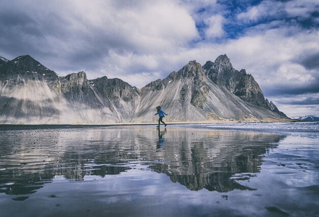 Persona con camisa azul y pantalón negro de pie en kayak azul en el lago cerca de la montaña debajo