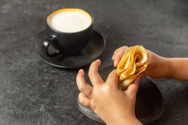 Persona comiendo panqueques enrollados con taza de leche en la oscuridad