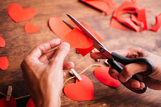 Persona cortando corazones de papel rojo