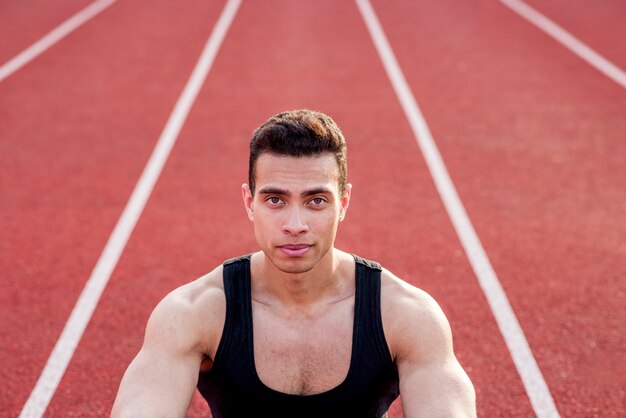 Persona de deporte muscular seguro en pista roja mirando a cámara