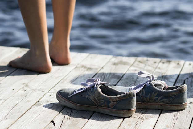 Persona descalza de pie cerca de los zapatos sucios en un muelle junto al mar