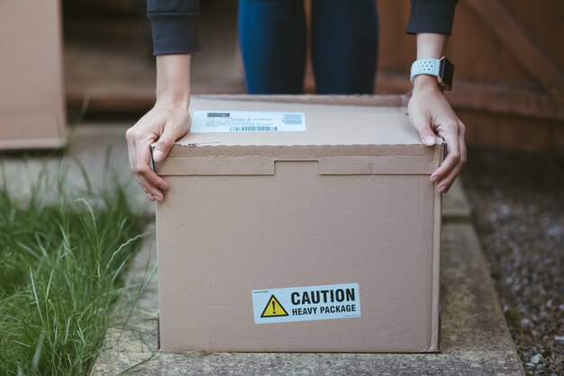 Persona descansando sus brazos sobre una caja de cartón con una etiqueta "precaución paquete pesado" en él