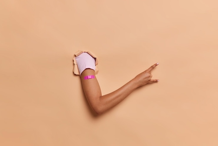 Foto gratuito persona desconocida muestra el brazo con yeso adhesivo después de recibir la vacunación muestra un gesto de rock n roll contra el fondo marrón del estudio concepto de vacuna e inmunización atención médica durante la pandemia