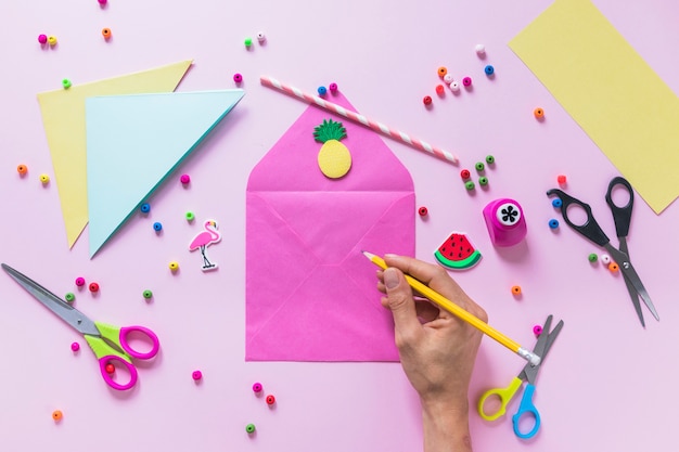 Foto gratuita una persona dibujando en el sobre con elementos decorativos sobre fondo rosa