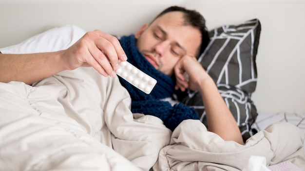 Persona enferma quedándose en la cama y mirando pastillas