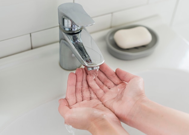 Persona enjuagarse las manos antes de lavarse con jabón