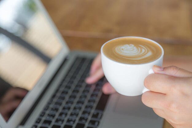 Persona escribiendo en un portátil sujetando una taza de café