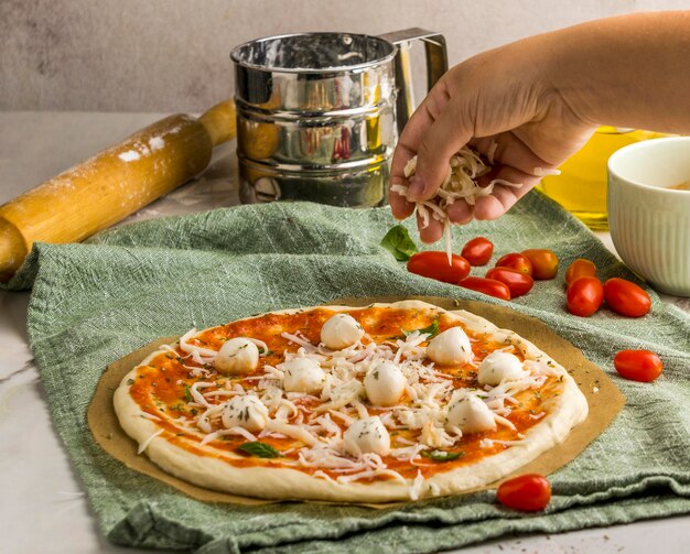 Persona espolvorear queso mozzarella sobre pizza