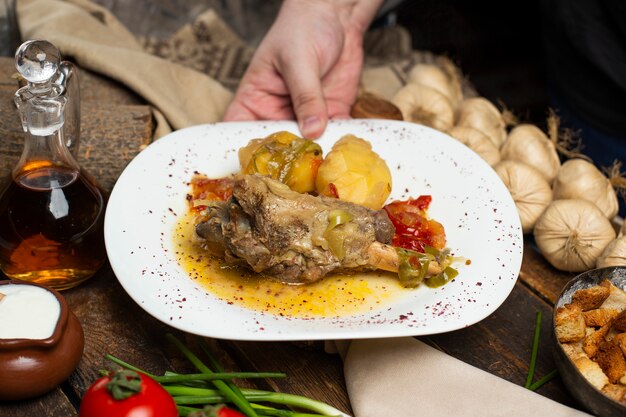 Una persona con estofado de carne con papas y caldo aceitoso en plato blanco en las manos.