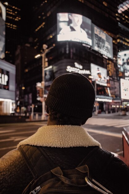 Persona con gorro de lana negro y chaqueta marrón de pie en la calle durante la noche