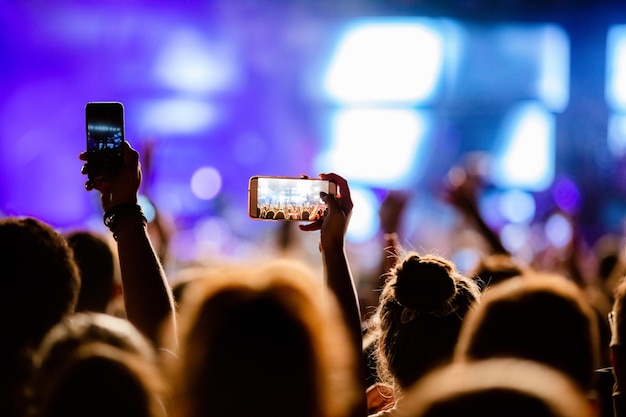 Persona irreconocible fotografiando con artistas de escenario de teléfonos inteligentes en festival de música