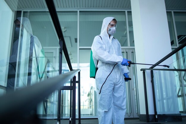 Foto gratuita persona irreconocible con traje de protección blanco desinfectando áreas públicas para detener la propagación del virus corona altamente contagioso