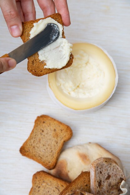 Persona irreconocible untando queso blando sobre pan tostado