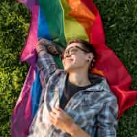 Foto gratuita persona joven alegre que miente en la bandera de lgbt en parque