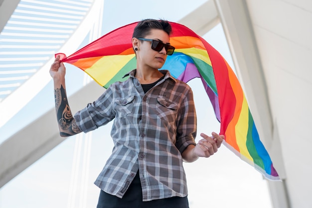 Persona joven manteniendo la bandera del arco iris revoloteando