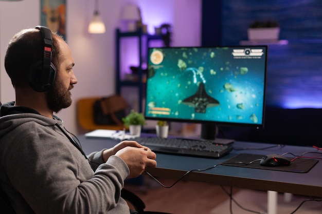 Persona jugando videojuegos con joystick y auriculares en la computadora. Reproductor con controlador y auriculares de audio para juegos en línea. Jugador con actividad divertida con equipo para jugar.