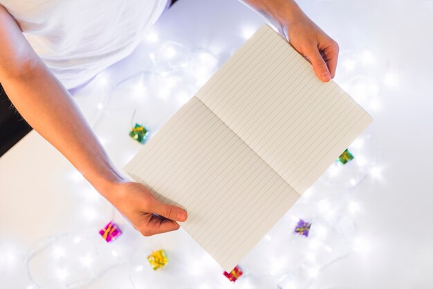 Persona con libro de escritura cerca de regalos y luces de colores.
