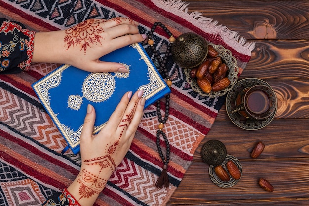 Persona con mehndi sosteniendo un libro de Corán cerca de una taza de té