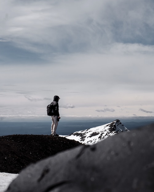 Una persona con mochila de pie en la cima de una montaña bajo cielo nublado