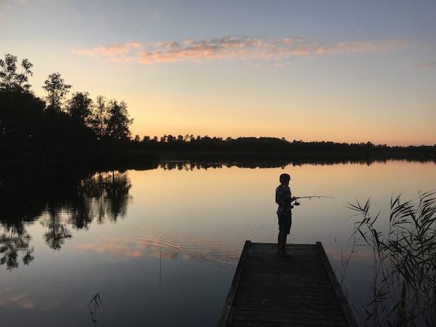Persona pescando desde el lago rodeado de árboles.
