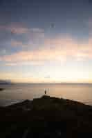 Foto gratuita persona de pie en la cima de una colina junto al mar al atardecer - concepto de éxito