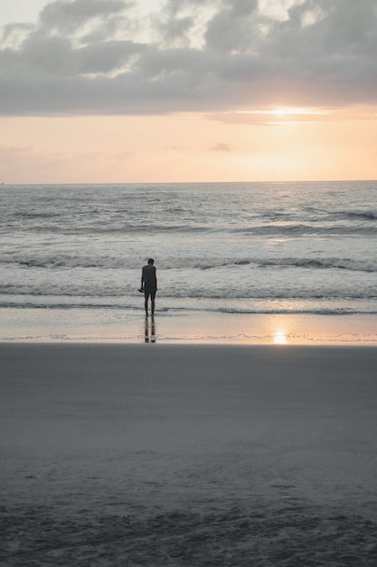 Persona de pie solo en la orilla de una playa con el reflejo de un sol poniente