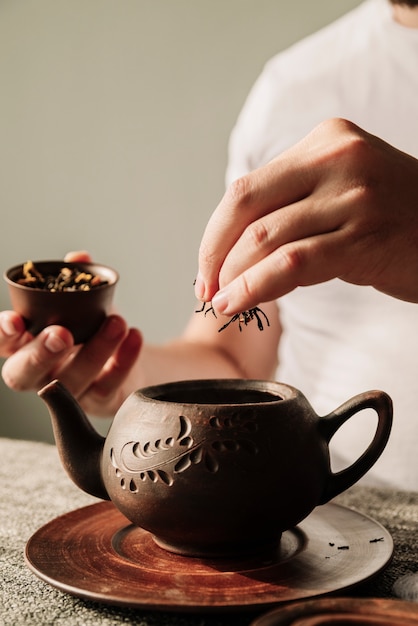 Persona poniendo hierbas de té en un primer plano de la tetera