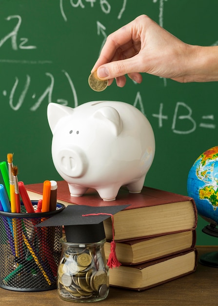 Persona poniendo monedas en la hucha con libros y gorra académica