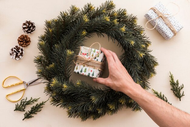 Persona poniendo una pequeña caja de regalo en corona de navidad