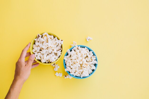 Persona poniendo tazón de palomitas de maíz amarillo cerca de azul