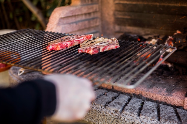 Una persona preparando carne a la parrilla en barbacoa