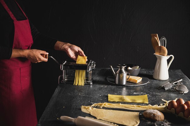 Persona de primer plano con delantal rojo y máquina de pasta