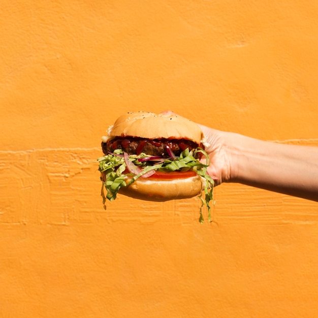 Persona de primer plano con hamburguesa y fondo naranja