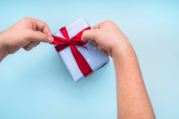 Una persona que ata la cinta en caja de regalo envuelta sobre el fondo azul