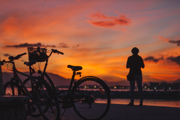 Persona que está parada en la bicicleta en puesta del sol