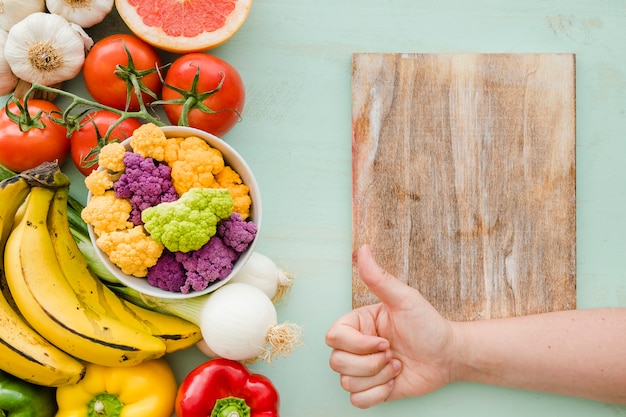 Una persona que muestra signo de Thumbsup sobre la tabla de cortar y comida sana fresca