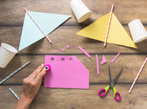 Una persona que perfora diseño floral en papel rosado sobre la mesa