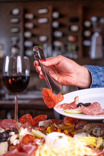 Persona que pone una variedad de surtido de carnes en el plato detrás de una copa de vino