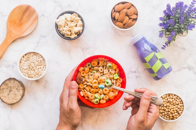 Persona que sostiene una cuchara con cereal encima de un tazón rojo