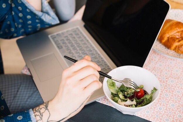 Persona que tiene ensalada con ordenador portátil en la mesa