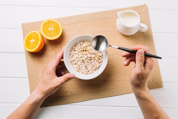 Persona que tiene harina de avena; mitad de naranja y leche en manteca de yute sobre superficie blanca