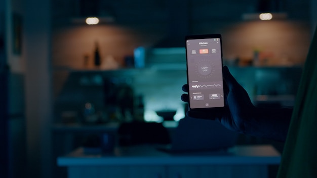 Persona que tiene un teléfono móvil con una aplicación de alta tecnología en una casa inteligente que controla las luces con un dispositivo inalámbrico