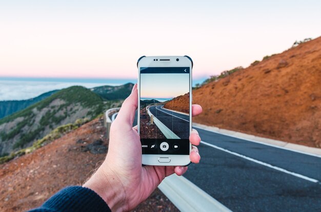 Persona que toma una foto de una carretera en una colina con su teléfono: ideal para fondos de pantalla