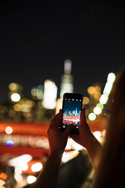 Persona que toma la foto de la ciudad de noche en el teléfono inteligente