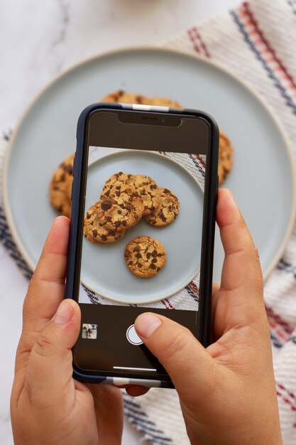 Persona que toma una foto de galletas con chispas de chocolate con un teléfono inteligente