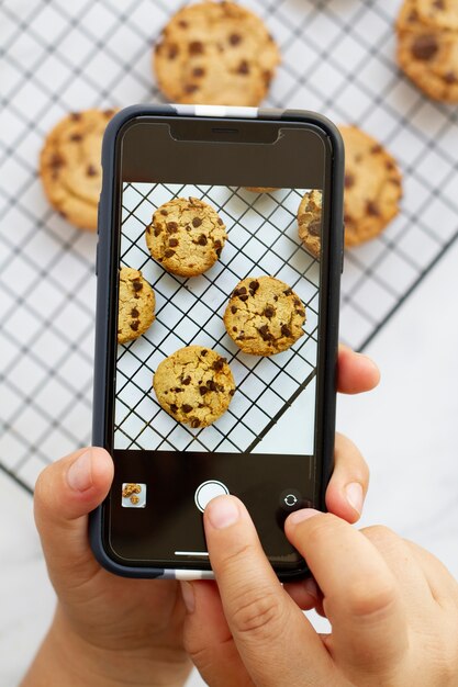 Persona que toma una foto de galletas con chispas de chocolate con un teléfono inteligente