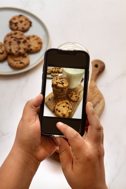 Persona que toma una foto de galletas con trocitos de chocolate y leche con un teléfono inteligente