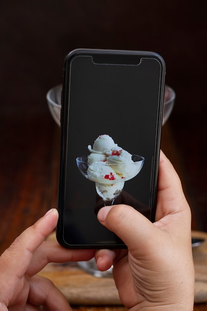 Persona que toma una foto de un helado en un vaso con un teléfono inteligente